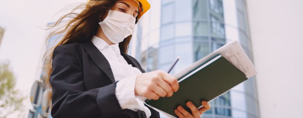 Girl builder with folder. Woman standing against the background of the city. Coronavirus theme.