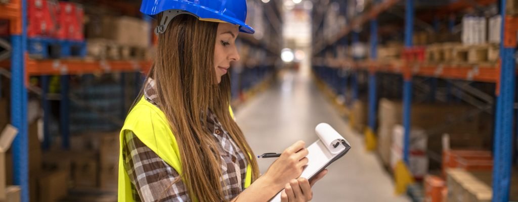 Portrait of female worker in distribution warehouse taking notes.